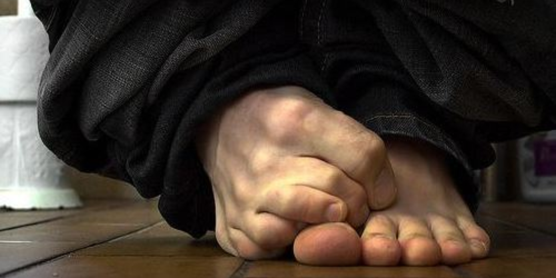 Bare feet with pant legs around ankles on a bathroom floor, toes curled and gripping the floor.
