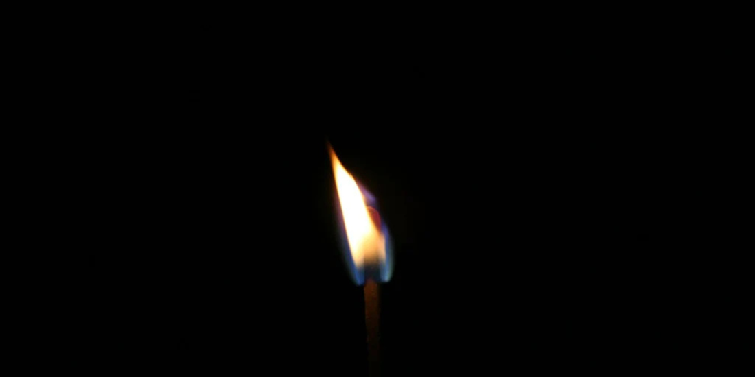 Single lit match with yellow-orange and blue flame against a black background.