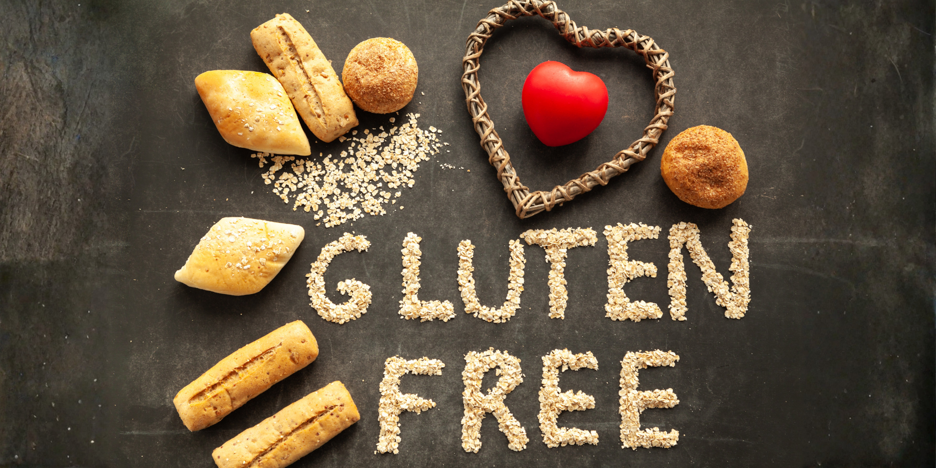 Assorted rolls and a red heart with GLUTEN FREE spelled in oats on a dark chalkboard surface