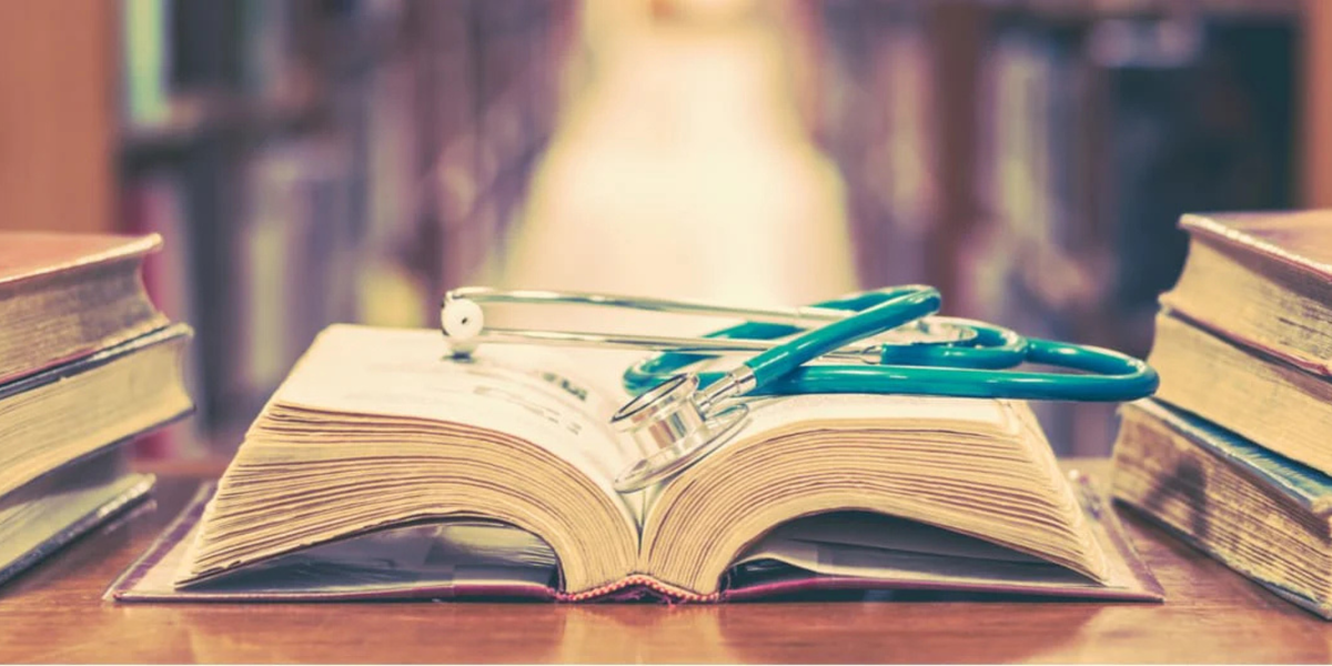 Open medical textbook with teal stethoscope resting across pages, evoking clinical or digestive health reference.