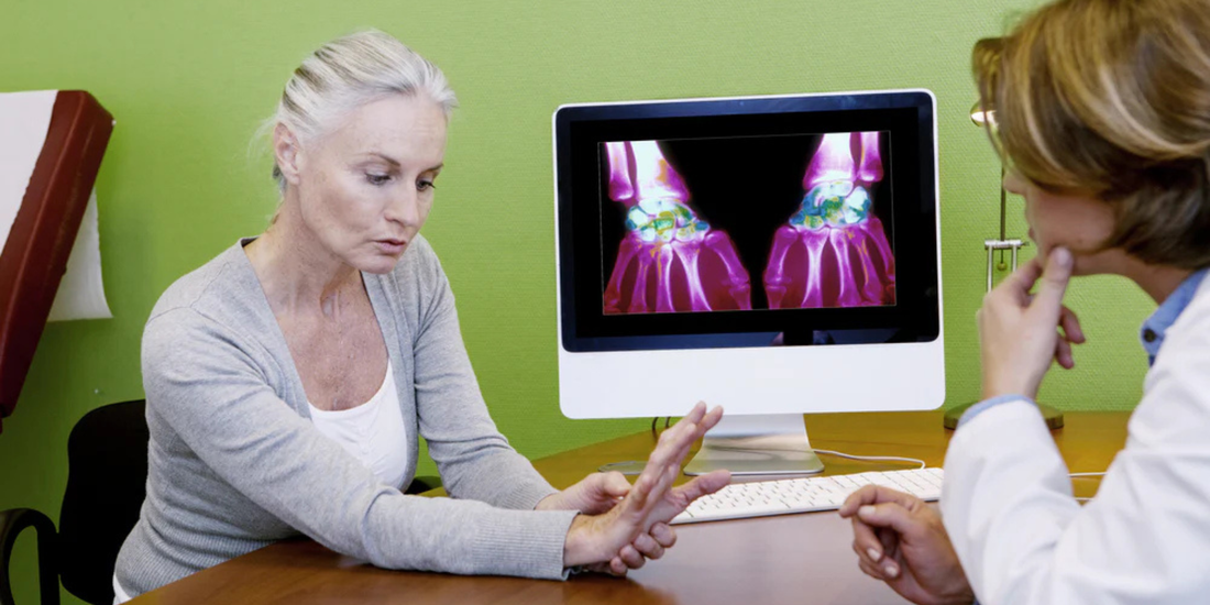 Older woman showing a painful wrist to a clinician with colored wrist scans visible on a computer monitor