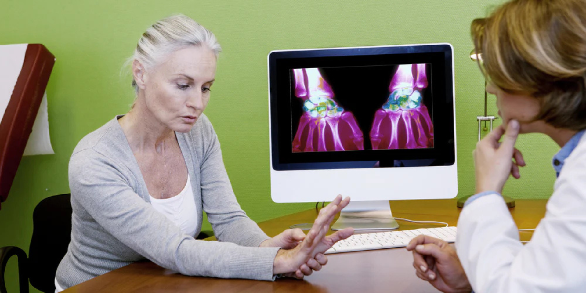 Older woman showing a painful wrist to a clinician with colored wrist scans visible on a computer monitor