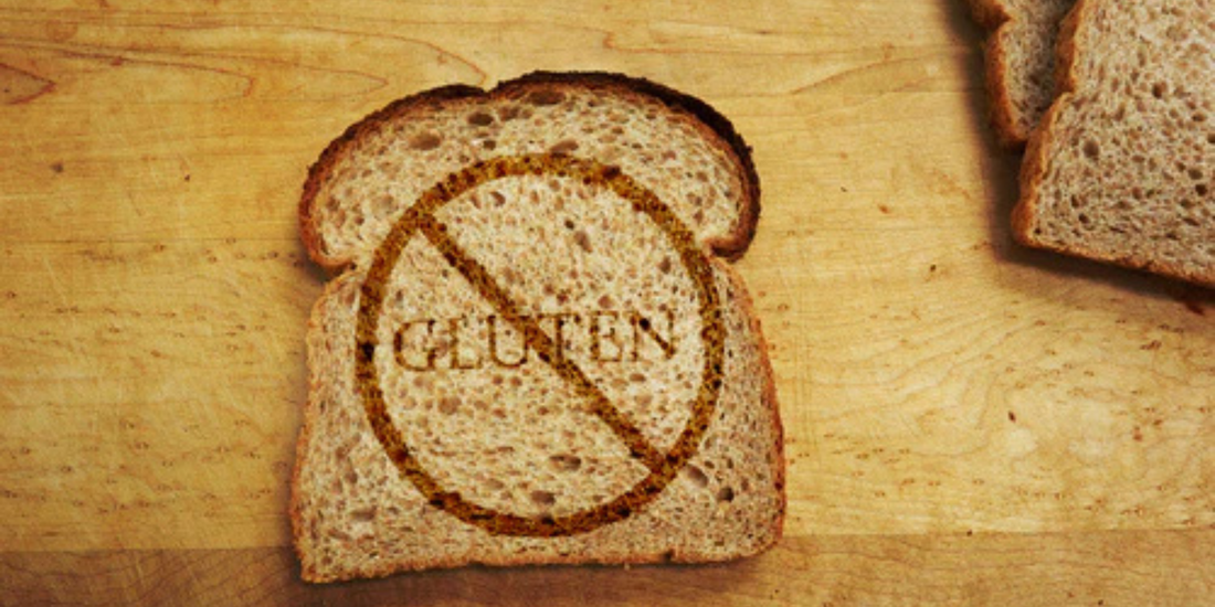 Slice of bread on wooden board with GLUTEN stamped and crossed out by a no symbol