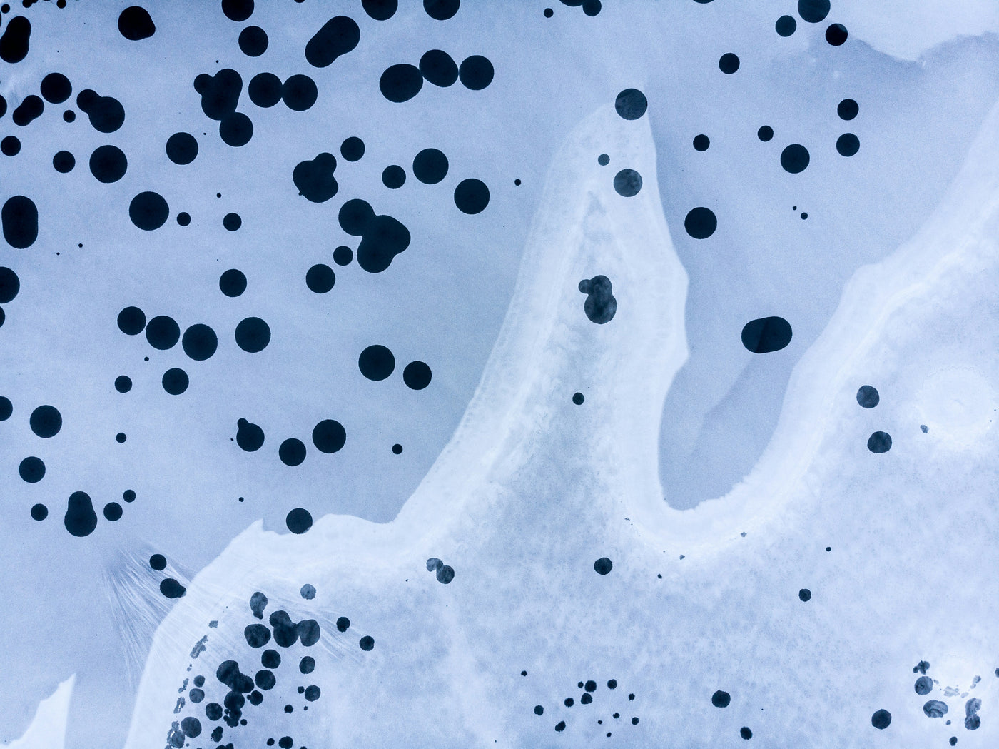Abstract blue shoreline with scattered dark circular droplets and ink-like blotches