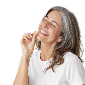 Smiling middle-aged woman with gray hair holding a yellow softgel vitamin near her mouth, eyes closed, wearing a white shirt.