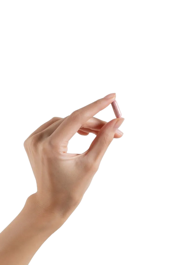 Hand pinching a small pink capsule between thumb and index finger against a black background.