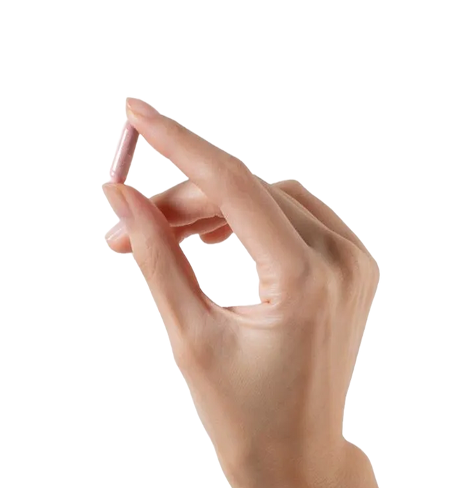 Hand holding a small pink capsule pill between thumb and forefinger
