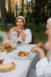 Smiling woman in a pink headscarf seated at an outdoor dinner table with plates, glasses, and companions.