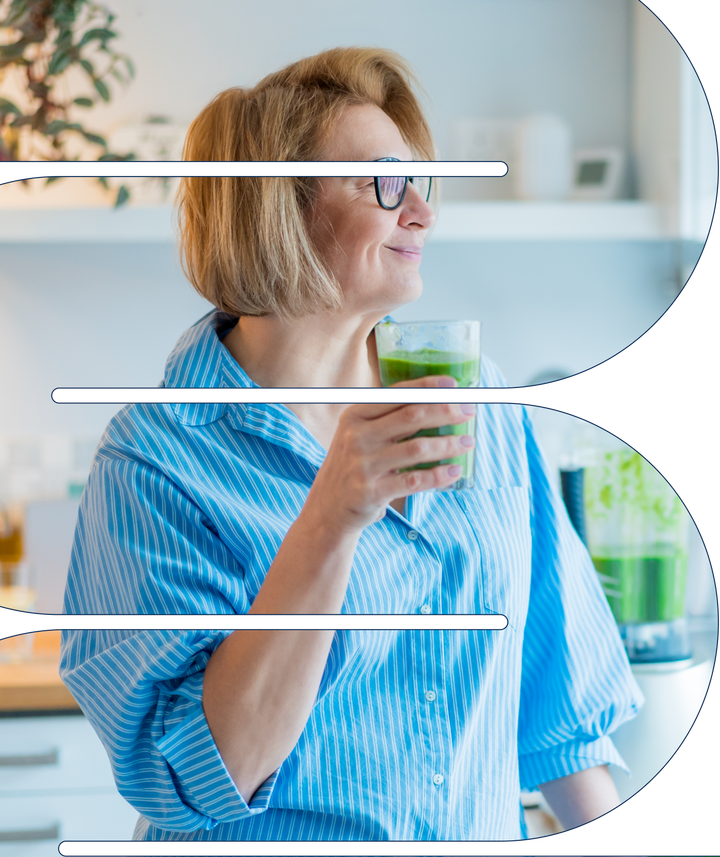 Woman in a striped blue shirt smiling and holding a green smoothie in a bright kitchen