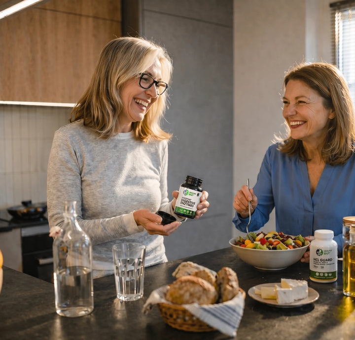 Two women smiling in a kitchen, one holding a Healthy Gut digestive enzymes bottle while they prepare a fruit salad
